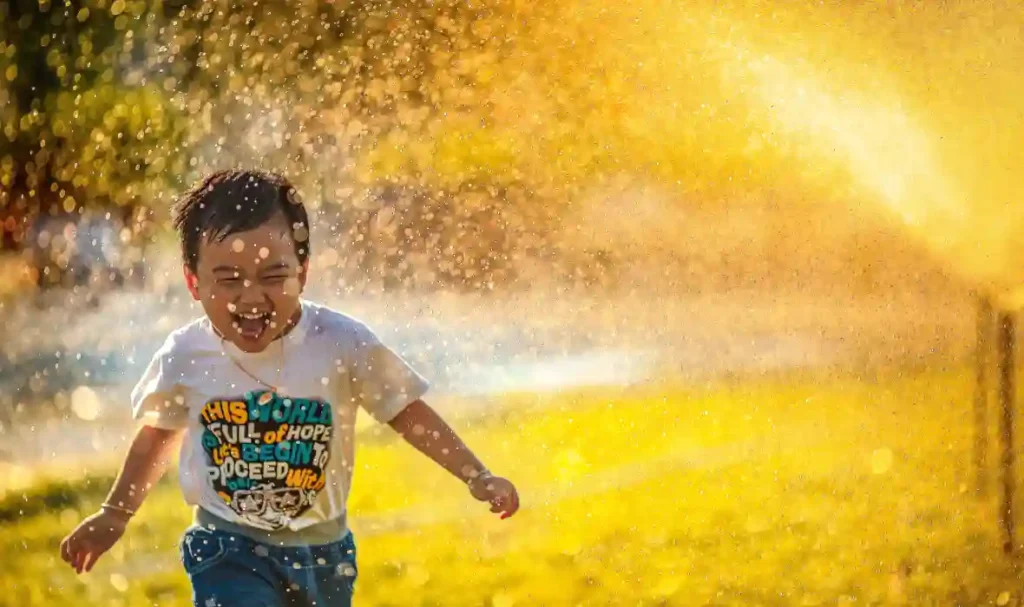 attività fisica per la salute dei bambini - bambino che corre sotto spruzzo d'acqua